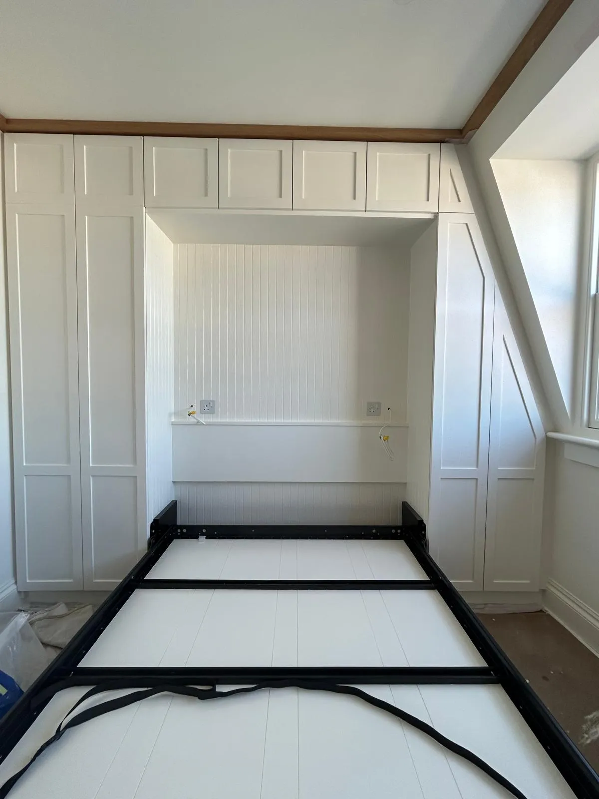 Shaker wardrobes round a bed recess, under a sloping roof: Doors hung and the headboard panelled