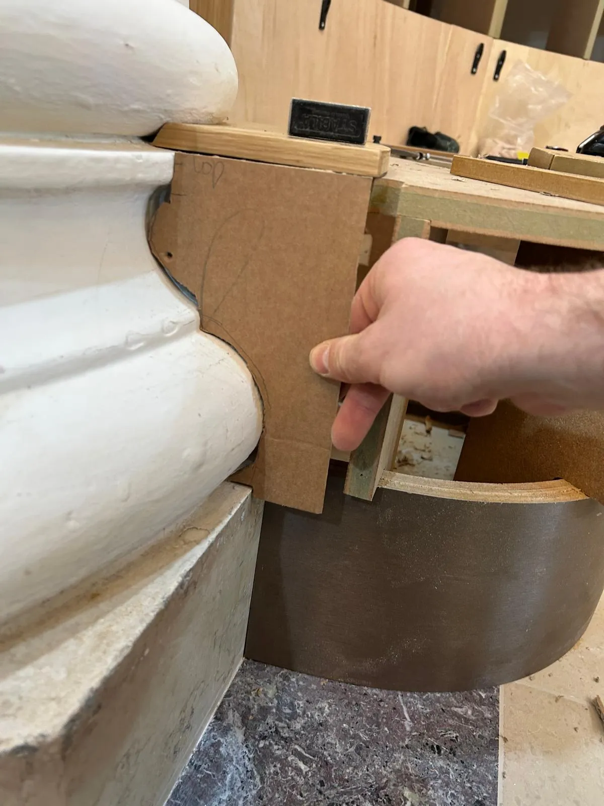 A hand holding a card template against the curved base of a column