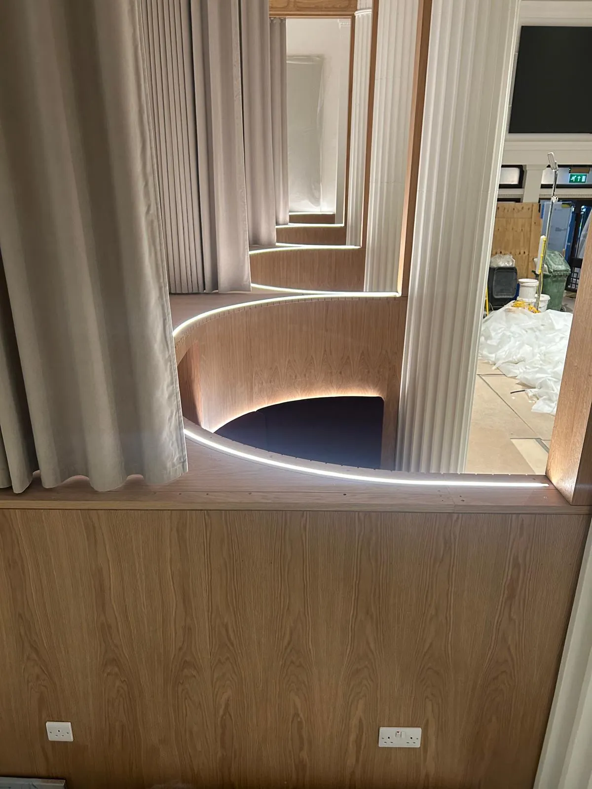 Curved oak panelling lit from below around an upholstered booth, next to a fluted column